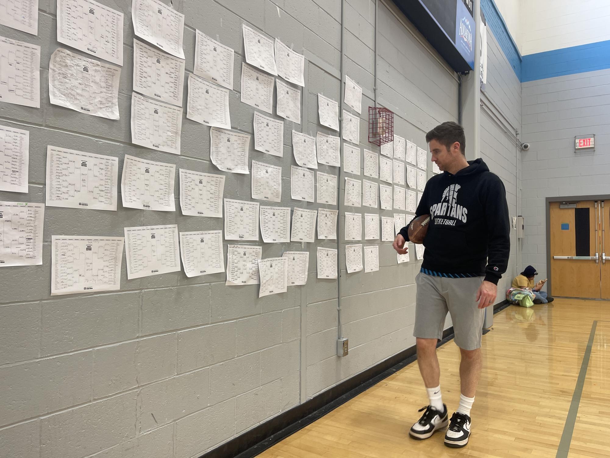 Community School of Davidson’s varsity women’s basketball coach, Matt Forrest, checks out one of the nearly 100 completed brackets hanging along the baseline of CSD‘s main gym. Picking winners and completing a bracket is a March ritual for both students and teachers.