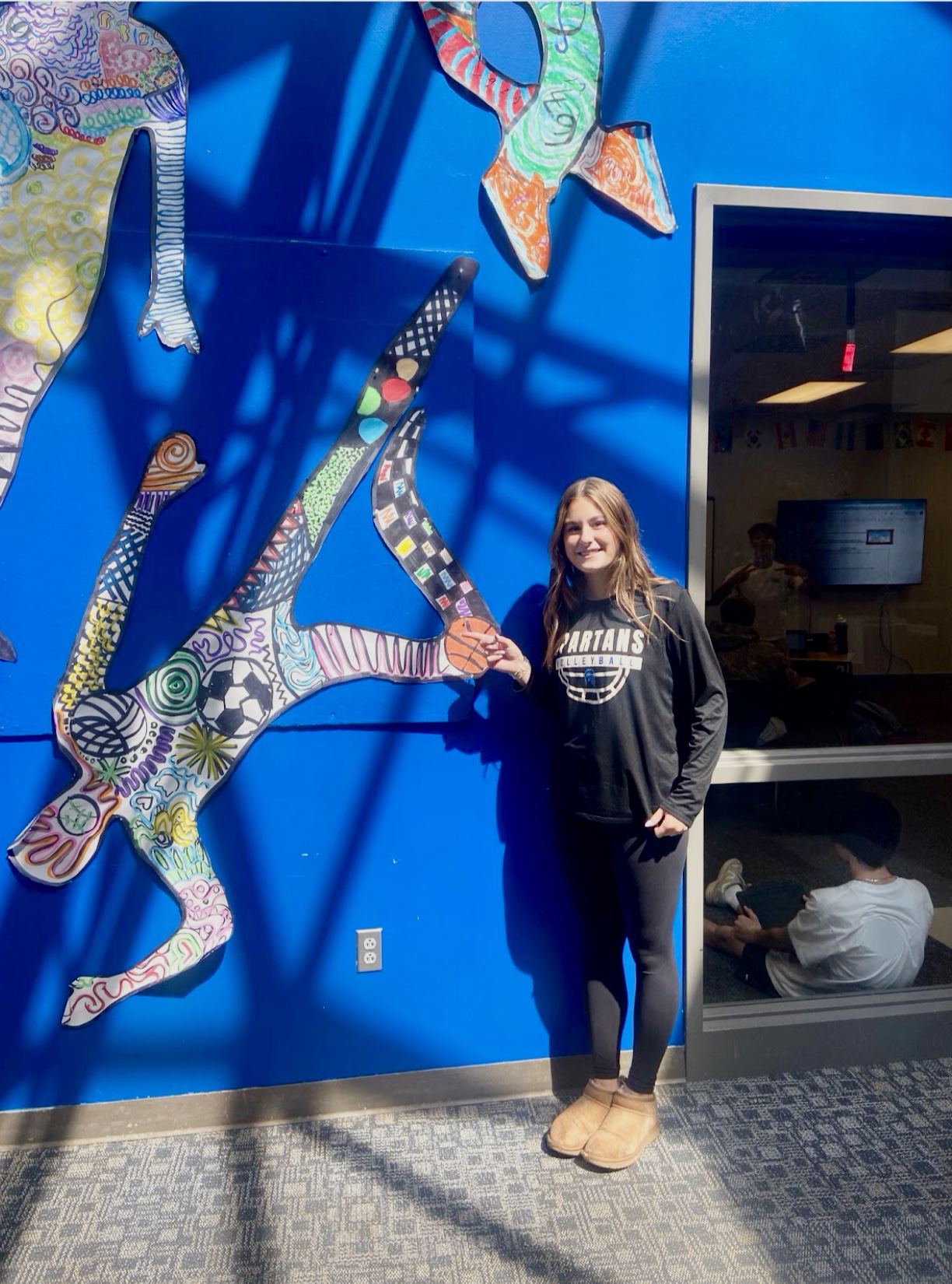Gracyn McRorie (‘26) stands next to her piece that she contributed to CSD Visual Arts’ first project of the year. Along with colors, lines and shapes, she added a volleyball and soccer ball to represent the sports she plays.            
