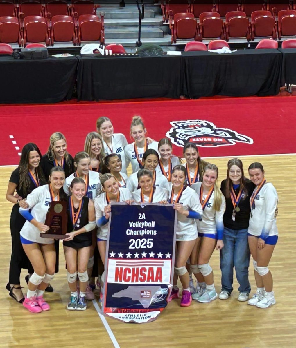 After the 3-0 victory, the Spartans Varsity volleyball team, along with the coaching staff, poses for a picture with their championship banner and the State Championship trophy. 
